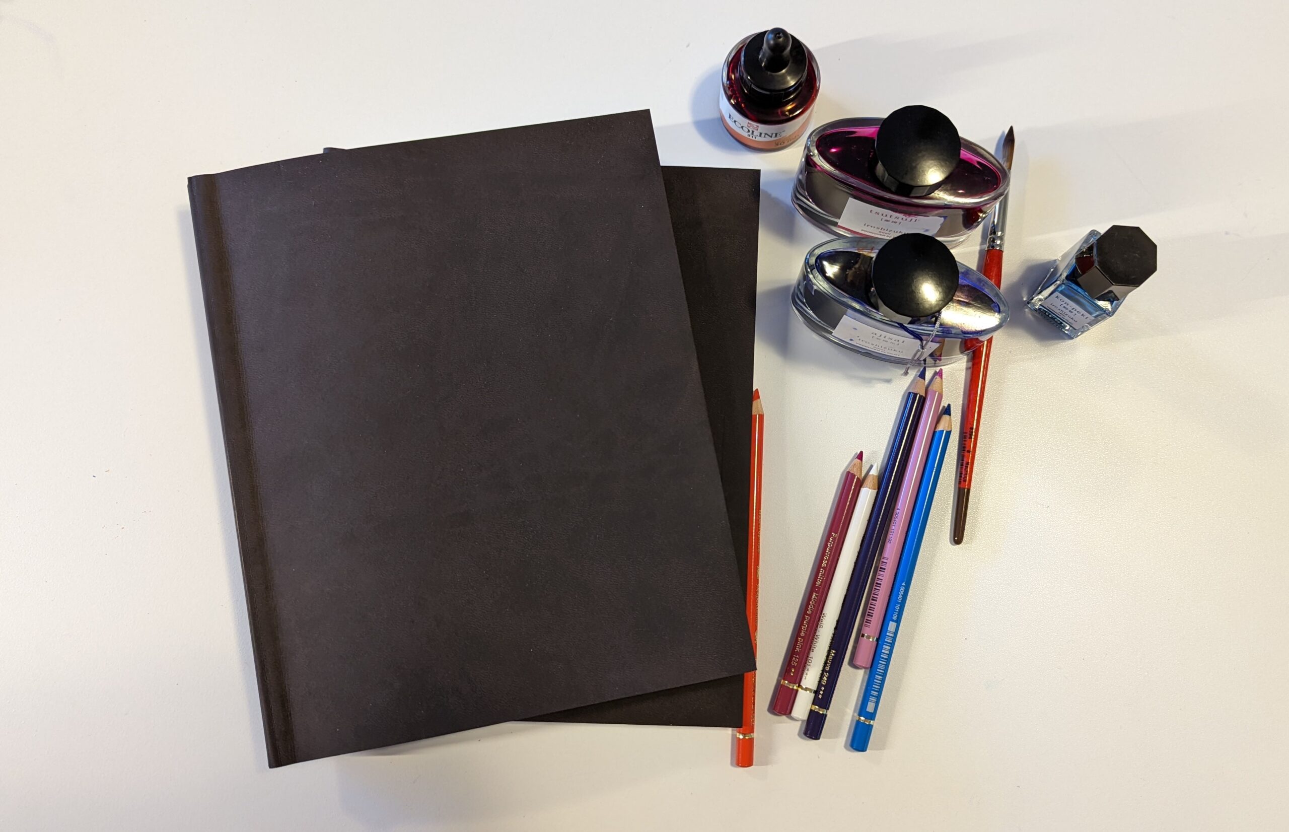 How to Fill your Sketchbook by Emi. Photo of a sketchbook with art supplies on a desk.